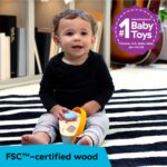A close-up of the Baby Einstein + Hape Discovery Radio Toy, a small wooden radio with a dial and flexible strap.